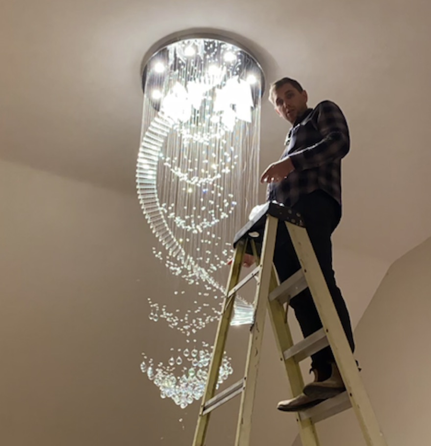 Taylor G, master electrician, installing a crystal chandelier in a Kingston home